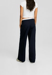 Marineblauwe gestreepte wijde broek met een platte tailleband, voorzien van achterzakken en een gladde textuur, gecombineerd met een witte cropped top.