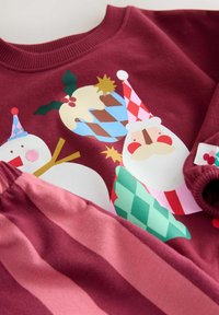 Bordový sweatshirt má farebnú grafiku Santa Clausa, snehuliaka a sviatočné prvky. Je doplnený o zladené nohavice s ružovými pruhmi. Mäkká textúra.
