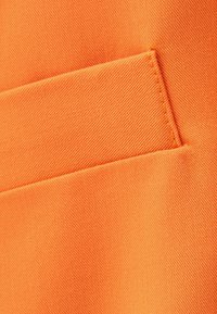 Ljust orange tyg med en välsydd passpoalficka, som visar textilens struktur och exakta sömdetaljer.