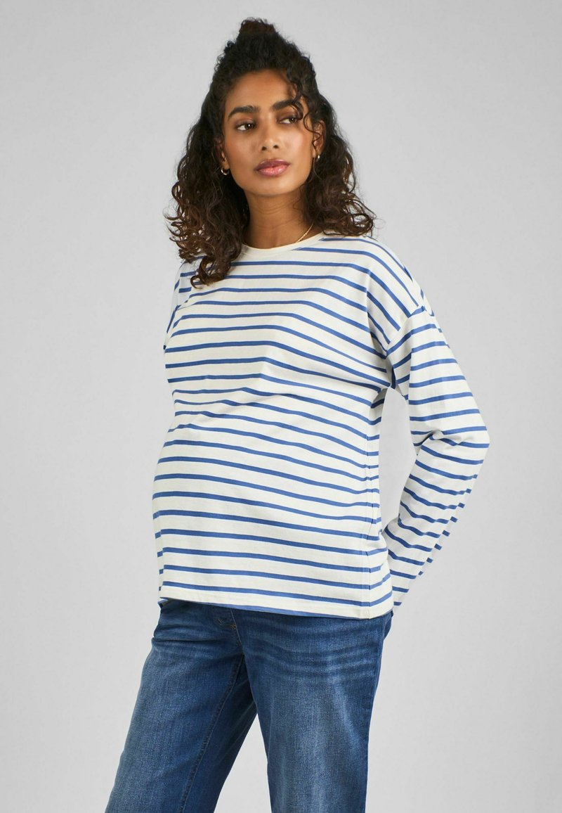 Maglietta premaman a maniche lunghe di colore crema con strisce orizzontali blu. Presenta una vestibilità comoda e un collo rotondo. Abbinata a jeans in denim.