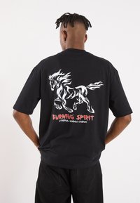 Black T-shirt featuring a white and flame-patterned horse graphic on the back. Text "BURNING SPIRIT" and "ETHERNAL SHADOW WISDOM" in red.
