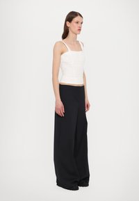 White cropped top with lace texture and square neckline, paired with high-waisted, wide-leg black trousers and black shoes.