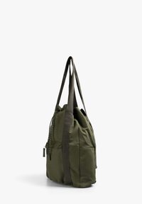Bolso tote de tela verde oliva con dos asas largas, cierre con cordón y dos bolsillos de parche laterales. Material texturizado con un acabado suave.