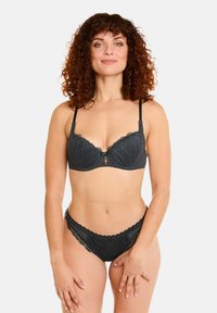 Soutien-gorge en dentelle noire et culotte assortie avec des motifs de feuilles, des bords festonnés, des bretelles réglables et un détail décoratif central sur le soutien-gorge.