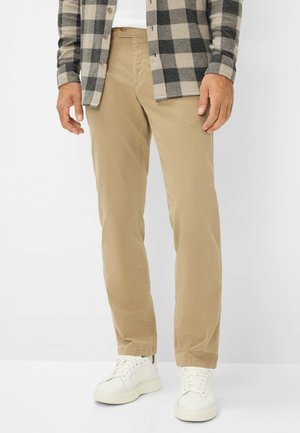Beige Baumwollhosen mit gerader Passform, kombiniert mit einem schwarz-grauen karierten Hemd und weißen Turnschuhen. Die Hosen verfügen über seitliche Taschen.