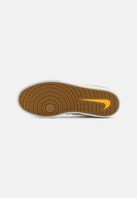 Sole boty Nike s vroubkovaným vzorem z gumy, s bílým okrajem a výrazným žlutým swooshem poblíž paty.