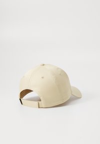 Beige baseball cap made of smooth fabric. Features a curved brim, stitched panels, and an adjustable strap at the back.