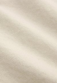 Crème-kleurige stof met een gestructureerd, geweven patroon. Het materiaal lijkt zacht en iets ribbelig, met subtiele variaties in tint.
