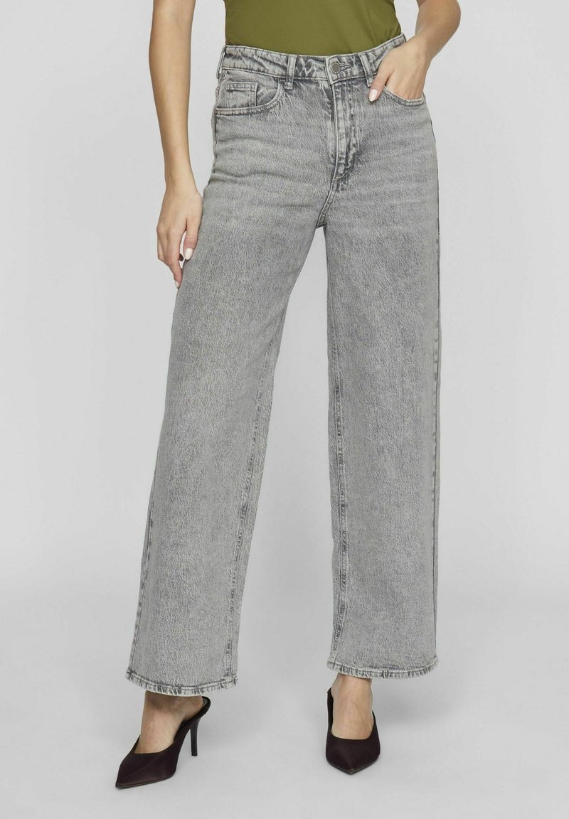 Jeans in denim grigio a gamba larga con vita alta, dotati di tasche frontali, una texture sbiadita e un orlo grezzo. Abbinati a tacchi a punta scuri.