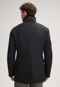 Cappotto di lana nera con colletto alto, caratterizzato da una finitura texturizzata e tasche laterali, mostrato dal retro su uno sfondo neutro.