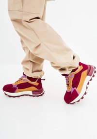 Sneakers multicolori in suede rosso, arancione e viola. Presentano una spessa suola bianca e una suola in gomma testurizzata con colletto imbottito.