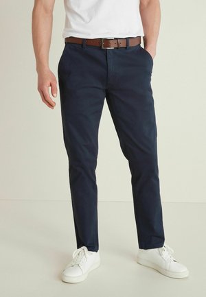 Chinos navy en coton avec une coupe slim, dotés de poches latérales et d'une ceinture en cuir brun, associés à des baskets blanches.