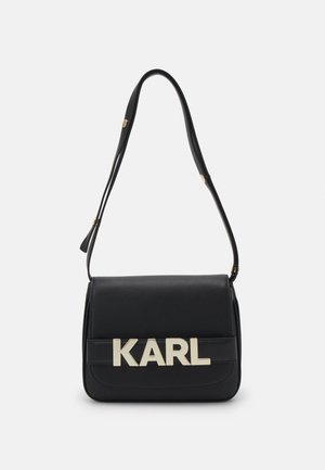 Borsa a spalla in pelle nera con logo dorato "KARL", forma rettangolare, chiusura a pattina piatta e tracolla regolabile. Texture liscia, design minimalista.