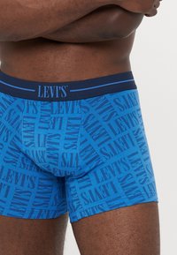 Kék boxeralsó, amelyet az egész felületén Levi's logó mintázat díszít, rugalmas derékrésszel és testhezálló fazonnal rendelkezik. Puha, rugalmas anyagból készült.