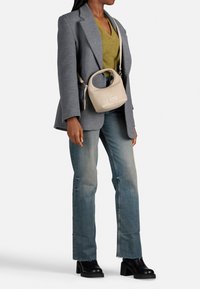 Borsa a tracolla in pelle beige con forma arrotondata, manico corto e hardware argentato, indossata su una maglia verde e sotto un blazer grigio.