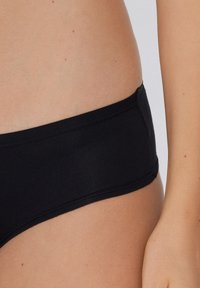 Czarne bawełniane majtki typu brief o średnim stanie, z bezszwowym pasem i miękką fakturą. Dyskretne przeszycia wzdłuż krawędzi.