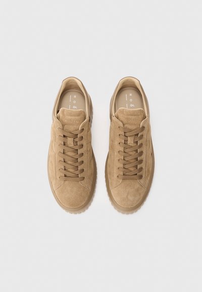 Pair of beige suede lace-up sneakers with thick rubber soles, viewed from above on a white background.