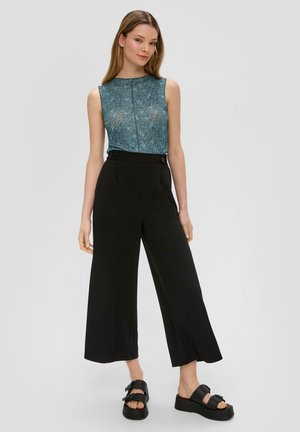 Teal sleeveless top with a textured pattern, paired with high-waisted black wide-leg trousers featuring button accents. Black platform sandals.