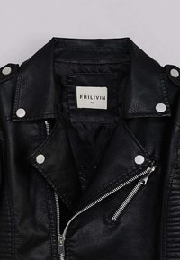 Veste de biker en similicuir noire avec des boutons-pression et des fermetures éclair argentés. Elle présente un col pointu et une étiquette à l'intérieur avec le nom de la marque et la taille.