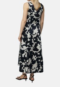 Ärmelloses Maxikleid in Marineblau mit weißem Blumenmuster. Glatter Stoff, A-Linie, mit V-Rücken und Seitentaschen. Schwarze Riemchenabsätze.