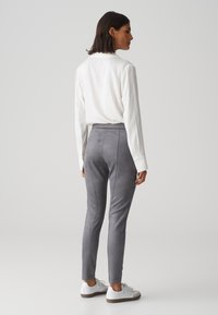 Graue Wildlederhosen mit taillierter Passform, elastischem Bund und glatter Textur, kombiniert mit einem weißen Langarmshirt und weißen Sneakern.