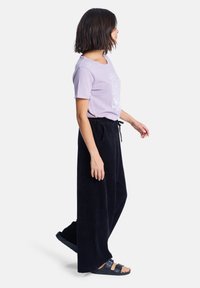 Hellblaues Baumwoll-T-Shirt mit Grafikdruck, kombiniert mit schwarzen Cord-Hosen im weiten Schnitt und schwarzen Riemchensandalen.