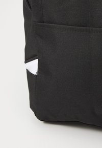Mochila de tela negra con un bolsillo lateral con un acento blanco, que presenta una superficie texturizada y un diseño simple.