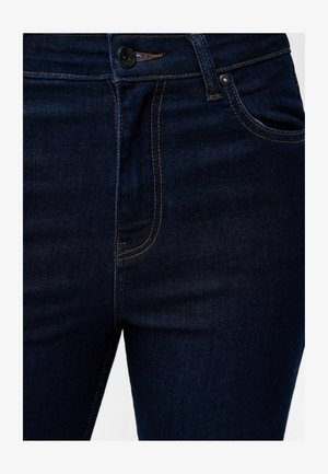 Jeans en denim bleu nuit avec des coutures orange. Les caractéristiques comprennent une fermeture à bouton, des poches avant et une coupe près du corps.
