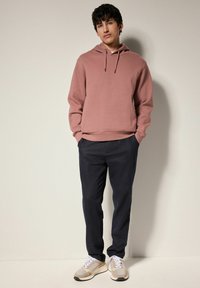 Sudadera texturizada de color rosa claro con cordón, combinada con pantalones oscuros de color marino y zapatillas beige con detalles grises. Un conjunto simple y moderno.