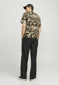 Chemise à manches courtes avec un motif floral beige et noir, associée à un pantalon noir et des baskets. La chemise a une coupe décontractée et un col.