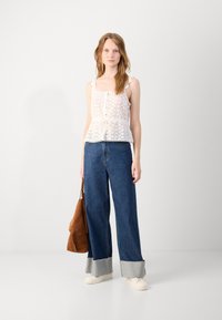 White, lace-trimmed top with buttons and a tie at the waist, paired with wide-leg blue denim jeans featuring a contrast cuff. Brown handbag.