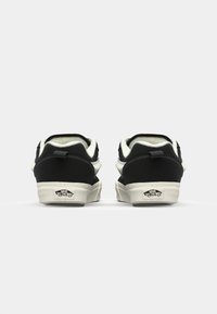 Černé semišové tenisky s bílou gumovou podešví a krémovým podšívem. Obsahují poutko na patě a logo Vans "Off the Wall" na patě.