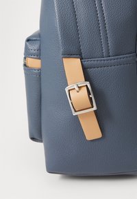 Niebieska torebka z teksturowanej sztucznej skóry z jasnobrązowym paskiem i srebrnym klamrą. Posiada przednią kieszeń i usztywnioną konstrukcję.