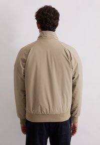 Beżowa kurtka typu bomber z wysokim kołnierzem, ściągaczami na mankietach i w pasie. Wykonana z gładkiego, lekkiego materiału o luźnym kroju.