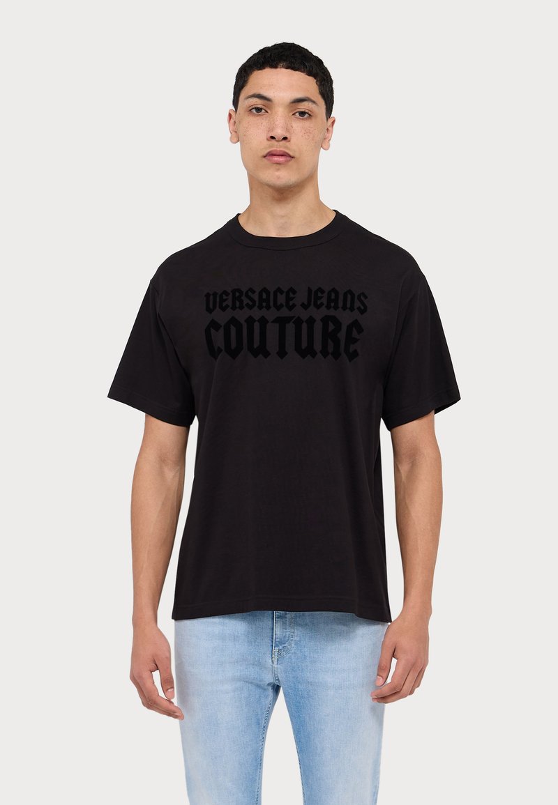 Tricou din bumbac negru cu text îndrăzneț "VERSACE JEANS COUTURE" într-un font stratificat. Mâneci scurte și decolteu rotund.