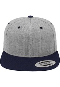 Grå snapback-cap med en solid mørkeblå skygge. Laget av tekstil med struktur, har seks ventilasjonshull og et rundt logemerke på skyggen.