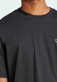 T-shirt en coton noir avec un col rond, des manches courtes et un logo discret sur la poitrine. Texture lisse et coupe classique.