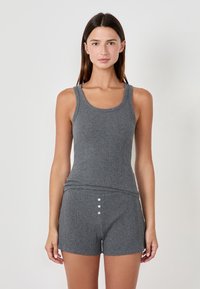Top sin mangas gris con textura de canalé y tirantes anchos, combinado con pantalones cortos a juego que presentan tres botones decorativos en la cintura. Textura suave.