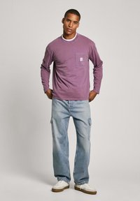 Lavender long-sleeve shirt with a chest pocket, paired with light blue cargo jeans and white sneakers with brown soles.