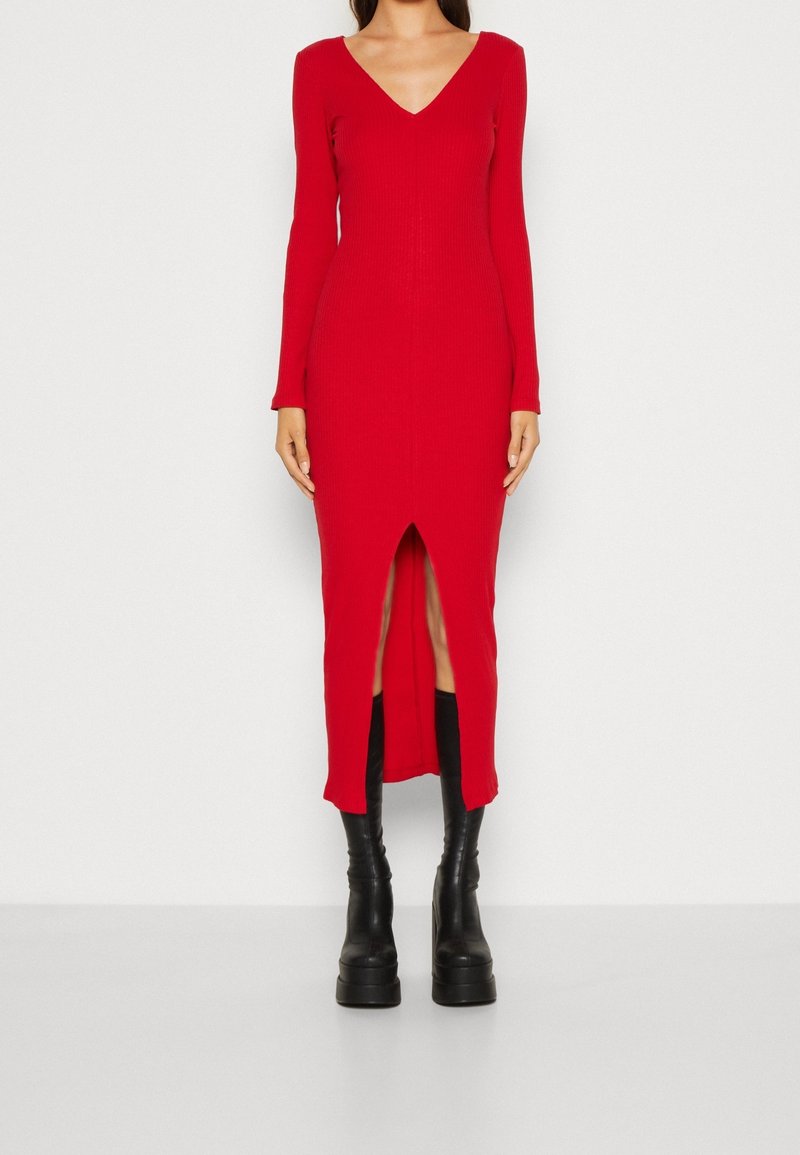 Femme portant une robe rouge en maille côtelée à manches longues avec une fente à l'avant, associée à des bottines noires épaisses à plateforme.