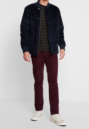 Námořnická manšestrová bunda s kulatým límečkem, pruhované tričko pod ní, vínové manšestrové kalhoty a bílé tenisky.