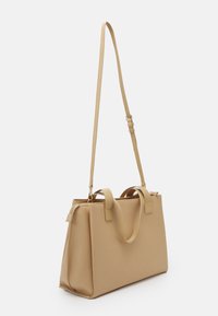 Beige textured tote bag with two top handles, an adjustable shoulder strap, and a zip closure. Smooth, structured shape with minimal hardware.