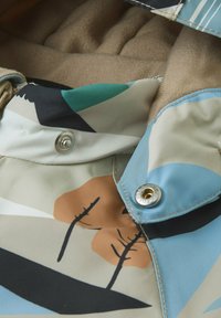 Stoffjacke mit einem mehrfarbigen abstrakten Muster in Blau-, Beige- und Brauntönen. Mit silbernen Druckknöpfen und einem weichen Innenfutter ausgestattet.