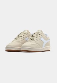 Μπεζ σουέντ αθλητικά παπούτσια με λευκές λεπτομέρειες, στρογγυλή μύτη, υφασμένο καουτσούκ πέλμα και απλό σχέδιο με κορδόνια. Κλασική αθλητική εμφάνιση με ελάχιστη επωνυμία.