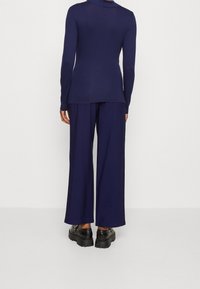 Marinblå långärmad topp med en lätt drapering, tillsammans med vida marinblå byxor. Båda i ett mjukt tyg. Svarta platåskor synliga.