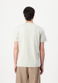 Light green short-sleeve t-shirt with a crew neck and slight texture, featuring a V-shaped back yoke and straight hem. Worn with beige pants.