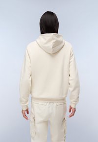 Felpa color crema con cappuccio regolabile, polsini e orlo a costine. Chi la indossa ha anche pantaloni cargo color crema con tasche a pattina.
