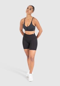 Musta urheiluliivi ja korkean vyötärön shortsiasu. Liivissä on syvä pääntie ja säädettävät olkaimet; shortseissa on tiukka malli, jossa on sileä pinta.