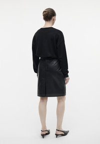 Zwart cropped sweater met lange mouwen, gecombineerd met een zwarte leren pencil skirt met een split aan de achterkant. Het model draagt zwarte hakken.