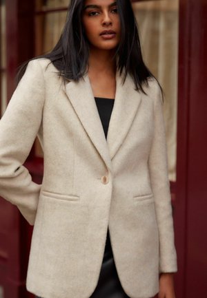 Blazer in lana beige con colletto a rever, chiusura a un bottone e due tasche frontali. Texture liscia e vestibilità su misura.